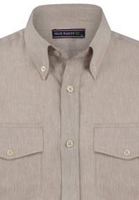 Camisa de botón beige clara hecha de un tejido texturizado, con un pequeño cuello, dos bolsillos en el pecho y botones beige. Etiqueta de la marca en el escote.
