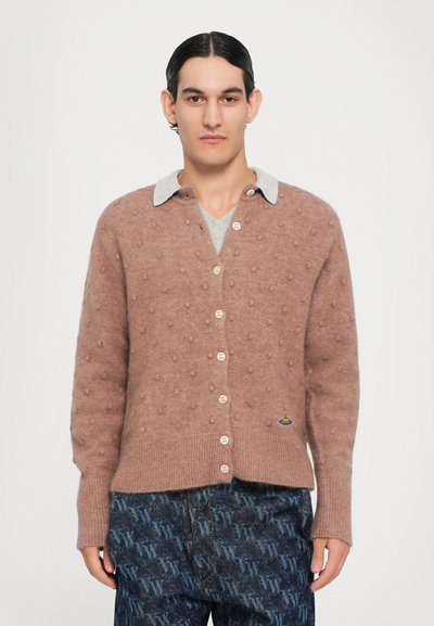 Cardigan castanho tricotado com textura de bolinhas, apresentando um colarinho cinza-claro e botões, combinado com calças escuras com padrão.
