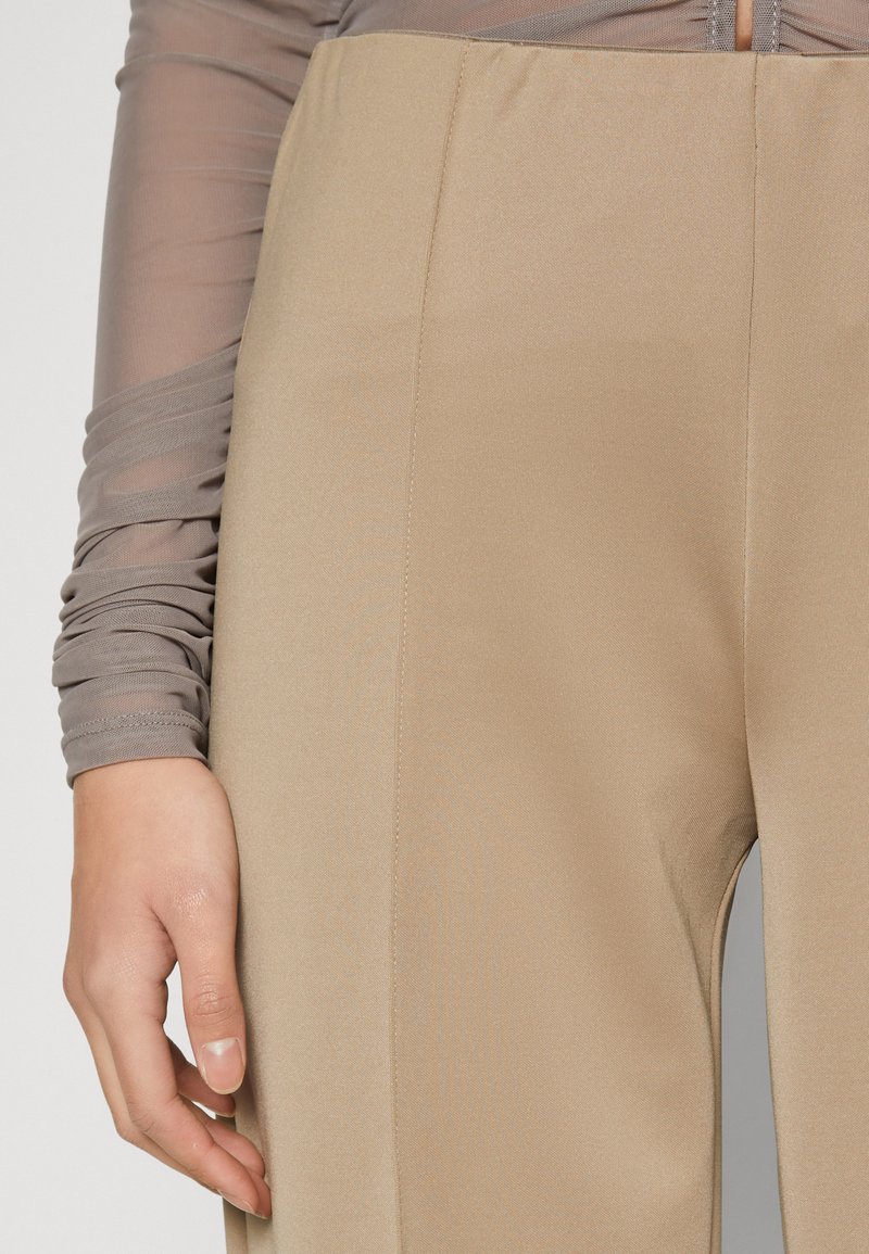 Beige, hochtaillierte Hose aus glattem Stoff mit Seitennähten und figurbetontem Schnitt. Graues, strukturiertes Oberteil mit langen Ärmeln und gerafften Ärmeln.