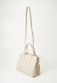 Beige texturerad handväska med präglat logomönster, dubbla handtag på toppen och ett avtagbart axelband. Har en strukturerad form och slät yta.