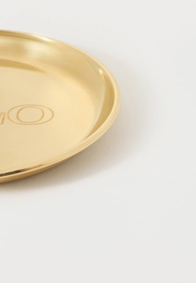 Στρογγυλό δίσκο από μεταλλικό υλικό με χρυσό χρώμα, με ανυψωμένο χείλος, που εμφανίζει μερικά ανάγλυφα γράμματα σε λευκό φόντο.