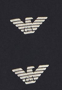 Černá tkanina s dvěma kovovými stříbrnými logy s křídly. Loga obsahují horizontální pruhy a pod nimi písmena "GA".