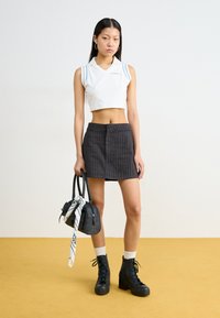 White cropped polo with blue stripes, gray pinstriped skirt, black platform boots, and a black bag with a patterned scarf. Yellow background.