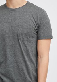 Grå kortærmet t-shirt lavet af blødt stof, med rund halsudskærm og en lille brystlomme. Tidsløs og minimalistisk design.