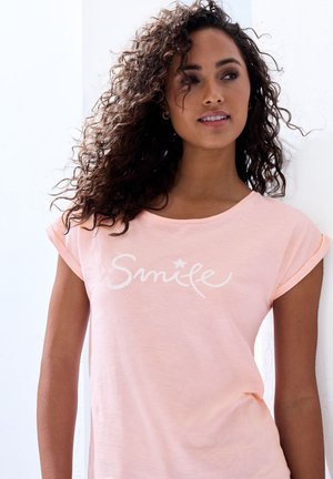 Lichtroze t-shirt met korte mouwen en opgerolde mouwen, witte "Smile" tekstontwerp, zachte textuur, ronde halslijn en relaxte pasvorm.