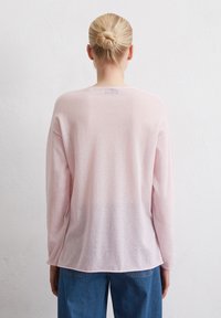 Helles pinker, langärmliger Pullover mit lockerer Passform, Rundhalsausschnitt und leicht transparenter Textur, kombiniert mit blauen Denimhosen.