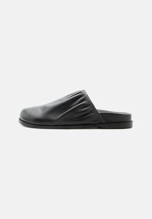 Black leather slip-on shoe with gathered detail on upper and flat sole, shown from side on plain background.