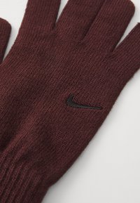 Guanti a maglia color mogano con texture a coste, dotati di un piccolo logo Nike nero nell'area del polso. Design a cinque dita per una copertura completa della mano.