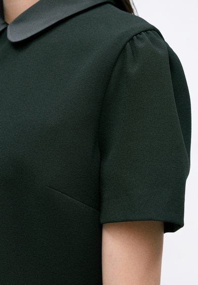 Rochie verde închis, cu guler rotunjit, mâneci scurte tip bufant și un material neted, texturat, cu un luciu subtil.