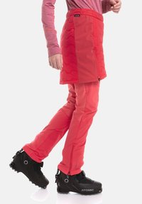 Punainen eristetty hame, jossa tikattu kuvio, yhdistetty vastaaviin punaisiin housuihin. Jalassa mustat laskettelumonot. Tausta on yksivärinen valkoinen.