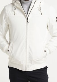 Witte gewatteerde jas met een ritssluiting aan de voorkant, een capuchon met trekkoord en zijzakken. Voorzien van zilverkleurige details en een geribde zoom en manchetten.