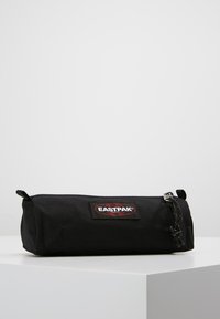 Astuccio nero in tessuto con chiusura a zip, caratterizzato da un'importante etichetta con il logo Eastpak rosso e bianco su un lato. Forma cilindrica, texture liscia.