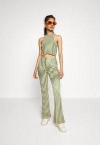 Conjunto em duas peças riscado em verde, amarelo e vermelho. Top cropped com alça de pescoço halter, calças largas e sapatos plataforma brancos chunky.