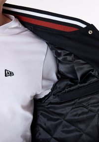 Black jacket with a ribbed collar featuring red and white stripes. Inside is quilted satin-like material. Worn over a white t-shirt.