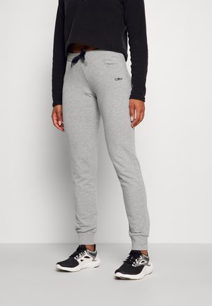 Persoon die lichtgrijze joggingsbroek met trekkoord draagt, zwart-witte sneakers en een korte zwarte top met lange mouwen, staand tegen een effen achtergrond.