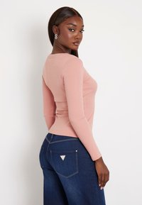 Ilga rankovė, ruoželinė koralinė palaidinė derinama su tamsiai mėlynomis plačiomis kelnėmis, kuriose ant užpakalinio kišenės yra mažas logotipas ir glausta silueto forma.