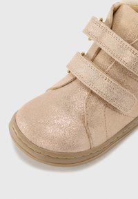 Bottines à paillettes roses en matériau texturé avec deux sangles Velcro et une semelle en caoutchouc ; présentent de subtils surpiqûres et un bout arrondi.