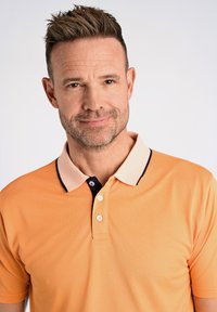 Pomarańczowa koszulka polo z kontrastowym kołnierzykiem w kolorze kremowym i granatowym, krótki rękaw i trzy guziki. Gładka faktura z dopasowanym krojem.