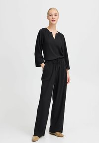 Completo due pezzi nero a costine con maniche lunghe e scollatura a V, caratterizzato da una vita con coulisse e pantaloni a gamba larga. Texture liscia in tutto il capo.
