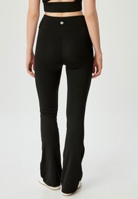 Zwarte flared leggings van rekbaar materiaal, met een hoge tailleband en een klein logo op de rug. Glad oppervlak en aansluitend ontwerp.