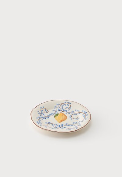 Assiette en céramique ronde avec motifs de fruits jaunes et de feuilles bleues, bords festonnés et un bord brun sur fond blanc.