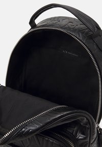 Zaino nero con un motivo testurizzato, chiusura con zip e manico superiore. L'interno presenta una fodera in tessuto liscio e un'etichetta interna.