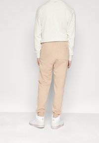 Beige joggbyxor med resårmidja, med sidostänger och en bakficka, kombinerat med vita sneakers. Mjuk bomullsmaterial.