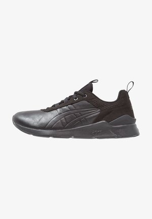 Chaussure de sport basse noire avec tige en cuir et mesh, fermeture à lacets, languettes sur la languette et le talon, et semelle épaisse texturée.