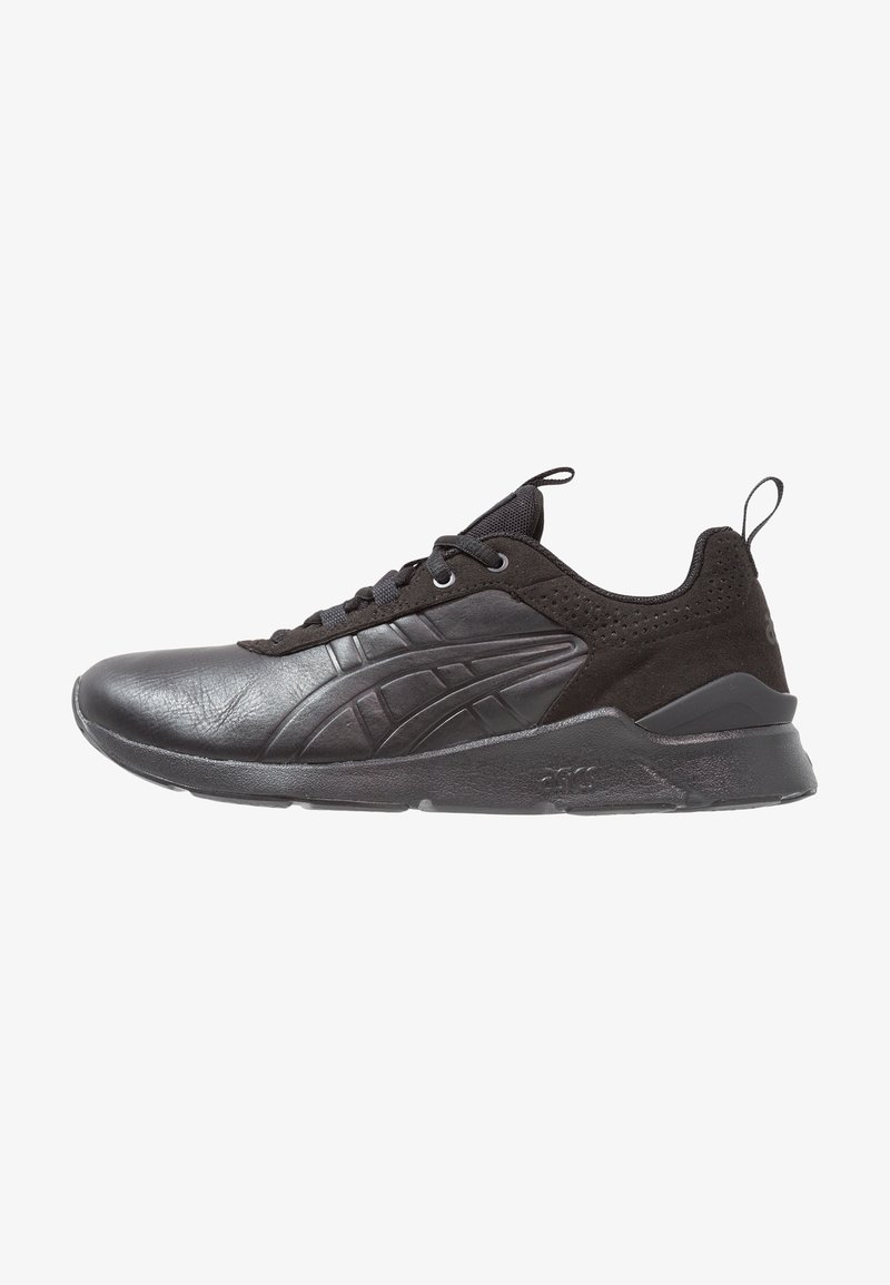 Chaussure de sport basse noire avec tige en cuir et mesh, fermeture à lacets, languettes sur la languette et le talon, et semelle épaisse texturée.