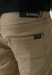 Khaki broek met een gestructureerde afwerking, voorzien van twee achterzakken en stoflabels met de merknaam "Garcia" in zwart en wit.