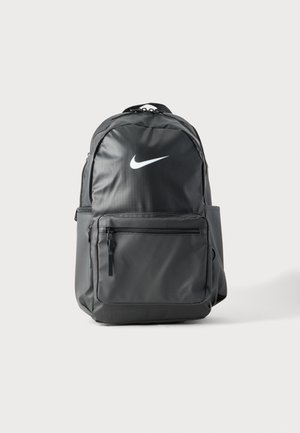 Sac à dos Nike noir avec poche zippée frontale, poches latérales, poignée supérieure et logo swoosh blanc sur un fond clair uni.