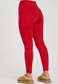 Leggings rouges avec une taille haute, un design ajusté et une texture lisse. Porté avec des chaussures tan à enfiler avec un accent duveteux.
