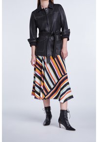 Veste en cuir noir avec taille ceinturée et surpiqûres contrastées, associée à une jupe midi rayée colorée et des bottines à lacets noires.