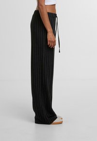 Čierne pruhované široké nohavice s elastickým pásom, mäkkou textúrou a voľným strihom. Nosené s ľahkou obuvou pre neformálny štýl.