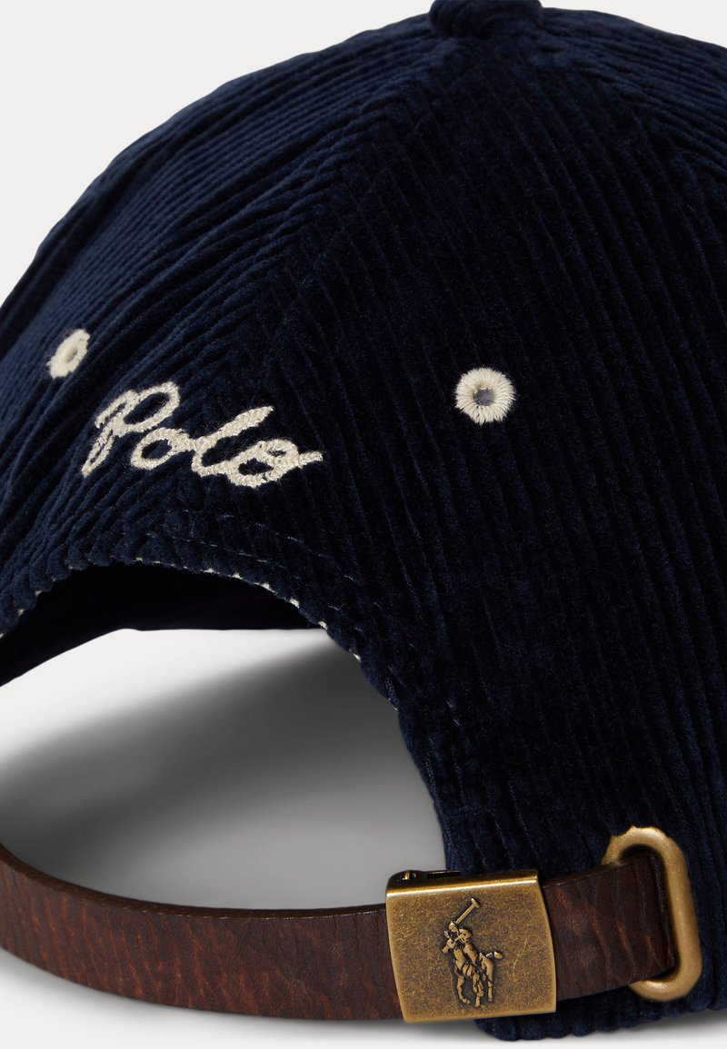 Marineblaue Cordhut mit strukturiertem Oberflächen, gesticktem "Polo"-Logo und braunem Lederband mit Messingverschluss und Logo-Akzent.
