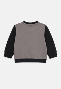 Siva i crna dukserica dugih rukava. Ima okrugli izrez, rebraste manžetne i kvadratnu oznaku na leđima. Izrađena je od teksturiranog materijala.