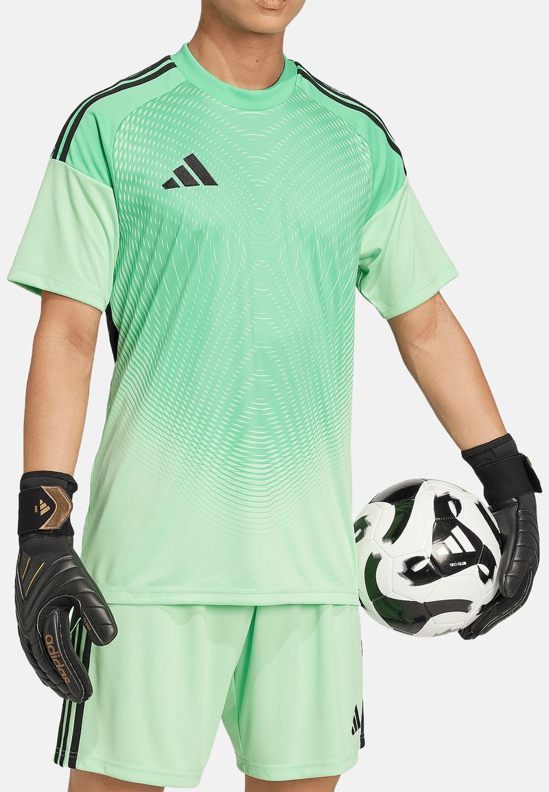 Grünes Fußballtrikot mit kurzen Ärmeln und schwarzen Akzenten sowie einem strukturierten Muster, kombiniert mit schwarzen Torwarthandschuhen. Ein schwarz-weißer Fußball wird gehalten.