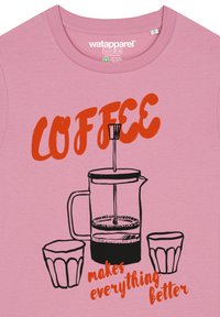 Roze t-shirt met een afbeelding van een koffiepers en twee kopjes, met de tekst "KOFFIE maakt alles beter" in vet rood.
