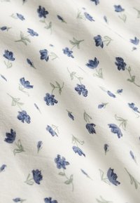 Witte stof met een patroon van kleine blauwe bloemen en lichtgroene stelen, gelijkmatig verspreid over het oppervlak.