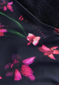 Virágmintás anyag, fekete háttéren rózsaszín orchideákkal, a felső széle mentén textúrált csipke részlettel. Logo látható.