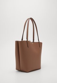 Sac fourre-tout en cuir marron avec une finition texturée, deux longues poignées, un haut ouvert et un accent métallique subtil à l'avant.