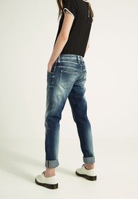 Blå denimjeans med en avslappnad passform, uppvikta fållar och subtila blekningar. Kombinerat med vita snörskor och en svart topp.