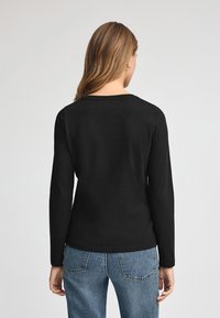 Schwarzes Langarmshirt mit Rundhalsausschnitt, glatter Textur, kombiniert mit hellblauen Jeans aus Denim mit Gesäßtaschen.