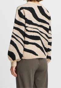 Pull en tricot beige avec des rayures noires de zèbre, présentant une coupe décontractée, des manches ballon et un col arrondi avec des poignets côtelés.