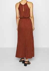 Maxi šaty v rezavé barvě s vertikálními černými pruhy, halter krk, elastický pas a otvor vzadu. V kombinaci s černými sandály na blokovém podpatku.