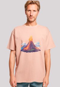 Light pink cotton t-shirt featuring a vibrant graphic of a volcano with orange lava, surrounded by clouds and mountains. Loose fit, short sleeves.