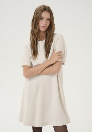 Beiges Kurzarmkleid mit rundem Ausschnitt, lockerer Passform und glattem Stoff, der bis zur Mitte des Oberschenkels reicht, getragen mit schwarzen Strumpfhosen.