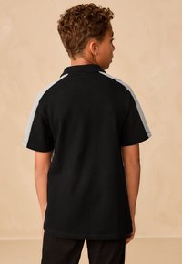 Černé polo tričko s krátkými rukávy, s světle šedými akcenty na ramenou. Vyrobeno z bavlněné směsi s texturovaným provedením.