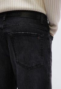 A fekete farmernadrág finoman texturált anyagból készült, bőr címkével, amelyen a "BOSS" márkajelzés látható, valamint oldalsó zsebrészlettel rendelkezik.