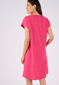 Abito a maniche corte in cotone rosa brillante, caratterizzato da una vestibilità ampia, scollo rotondo e lunghezza fino a metà coscia con spacchi laterali per facilitare i movimenti.